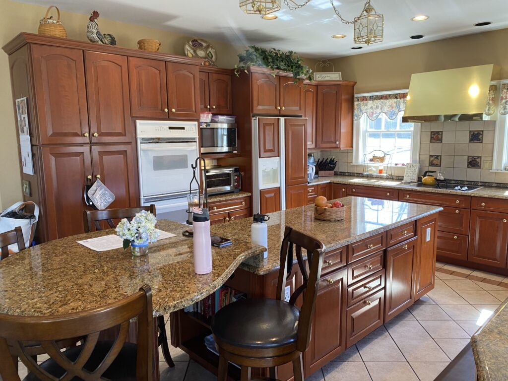 Remodeled kitchen with woodgrain cabinets, tan granite countertop, large island with one end rounded with stool seating. White tile floor, yellow/brown walls.