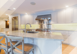 Renovated kitchen with white cabinets and white stone countertops, light wood floors, recessed lighting and under-cabinet lighting.