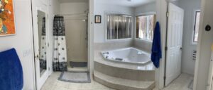 Accessibility-renovated bathroom with step leading up to large soaking tub, wide doorway, white tile floor, and walk-in shower.